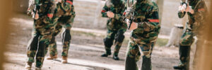 paintball team in uniform and protective masks playing paintball with marker guns outdoors